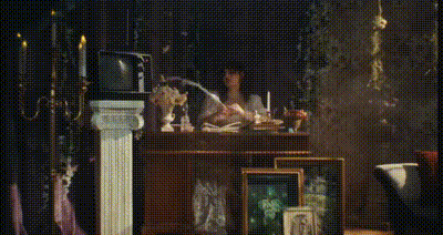 rachel bochner in a dress sitting at a desk, putting a feather pen on it